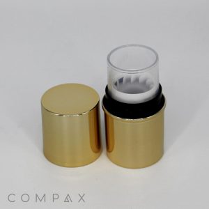 A gold-colored cylindrical container with its cap removed, revealing a transparent inner chamber. The container is set against a plain white background, with the brand name "COMPAX" visible at the bottom.