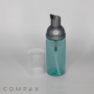 A 50mL Round PET Bottle with Foamer, featuring a transparent teal body and gray pump top. The bottle comes with a separate clear plastic cap placed beside it. "COMPAX" is displayed in gray, uppercase letters in the bottom-left corner.