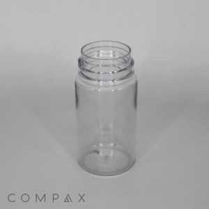 A clear, empty 100mL PET bottle with a foamer attachment stands upright on a plain surface. The open top shows visible threading for a cap, and the branding "COMPAX" is visible in the lower left corner.