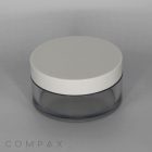 A round, transparent 50mL PET jar with a white short cap is central in the image. The container appears to be designed for holding creams or cosmetics. The word "COMPAX" is subtly printed in the lower left corner of the image. The background is plain and grey.