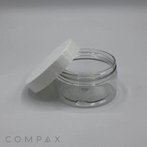 A clear, empty 120mL PET Jar with a white lid is displayed on its side. The lid is slightly tilted and leaning against the jar, providing a view of both the container and the lid. The background is plain and light-colored, with the word "COMPAX" visible at the bottom left corner.