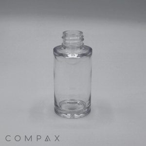 A 30 mL Heavy Wall PET Bottle, made of clear glass with its screw-top cap removed, standing upright on a smooth, light gray surface. The word "COMPAX" is visible in the bottom left corner of the image.