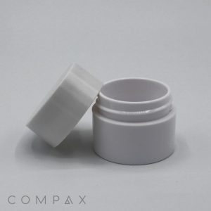 A small, white PET Jar with an unscrewed lid slightly tilted and placed to the side. The jar is empty and set against a plain, light gray background. The word "COMPAX" is faintly visible at the bottom left corner of the image.