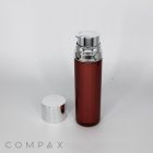 A sleek, cylindrical brown Round Airless Bottle with a metallic silver pump dispenser stands upright on a white background. The bottle features a removable silver cap placed beside it. The brand name "COMPAX" is visible at the bottom of the image.