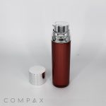 A sleek, cylindrical brown Round Airless Bottle with a metallic silver pump dispenser stands upright on a white background. The bottle features a removable silver cap placed beside it. The brand name "COMPAX" is visible at the bottom of the image.