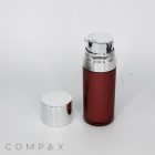 A sleek, cylindrical Round Airless Bottle with a metallic silver dispenser cap stands upright on a white surface. Next to it lies a detached silver cap. The bottle's body is a glossy shade of brown. The word "COMPAX" is subtly displayed in the bottom left corner of the image.
