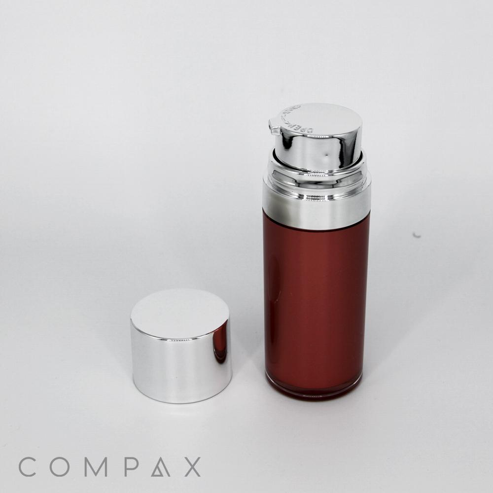 A sleek, cylindrical Round Airless Bottle with a metallic silver dispenser cap stands upright on a white surface. Next to it lies a detached silver cap. The bottle's body is a glossy shade of brown. The word "COMPAX" is subtly displayed in the bottom left corner of the image.