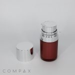 A sleek Round Airless Bottle with a shiny silver cap next to it. The bottle is partially filled with a reddish-brown liquid and features a silver dispensing pump on top. The background is plain white, and the word "COMPAX" is visible at the bottom left in gray text.