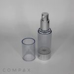 A Round Acrylic Airless Bottle with a silver nozzle and a transparent cap is placed beside it. The bottle's base and nozzle are metallic silver. The brand name "COMPAX" is visible in small letters at the bottom left corner of the image.