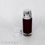 A metallic cylindrical container named "Round Dual Chamber Airless Bottle" with a shiny silver top and a transparent plastic cap placed beside it, featuring a dark brown body labeled "COMPAX" at the bottom left corner of the image. The background is plain white.
