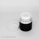A black and white cosmetic jar with a silver accent encircling the top, and a clear lid resting beside it. The word "COMPAX" is written in gray text at the bottom left of the image.