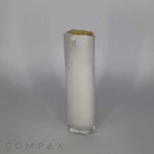 A tall, oblong airless bottle with a white substance inside. The bottle features a gold-colored cap on top. The image has the word “COMPAX” written at the bottom left corner.