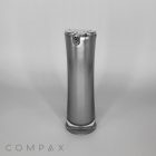 A tall, sleek Hourglass Airless Bottle in silver with a curved design, featuring a shiny finish and a small metallic clasp near the top. The word "COMPAX" appears in light grey at the bottom left corner of the image. The background is plain white.