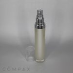 A frosted Round Airless Bottle with a silver cap and nozzle, containing a cream-colored product. The clear plastic lid is removed and placed beside the bottle against a neutral gray background. The word "COMPAX" is visible at the bottom left of the image.