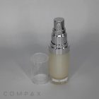 A sleek silver and clear Round Airless Bottle stands upright with a transparent cap removed and placed next to it. The bottle contains a light-colored liquid. The word "COMPAX" is faintly visible at the bottom left of the image. The background is neutral gray.