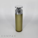 A slender, cylindrical "Round Airless Bottle" with a gradient design transitioning from olive green at the base to a frosted clear at the top. It features a shiny silver cap and is labeled "COMPAX" at the bottom left. The background is plain white.