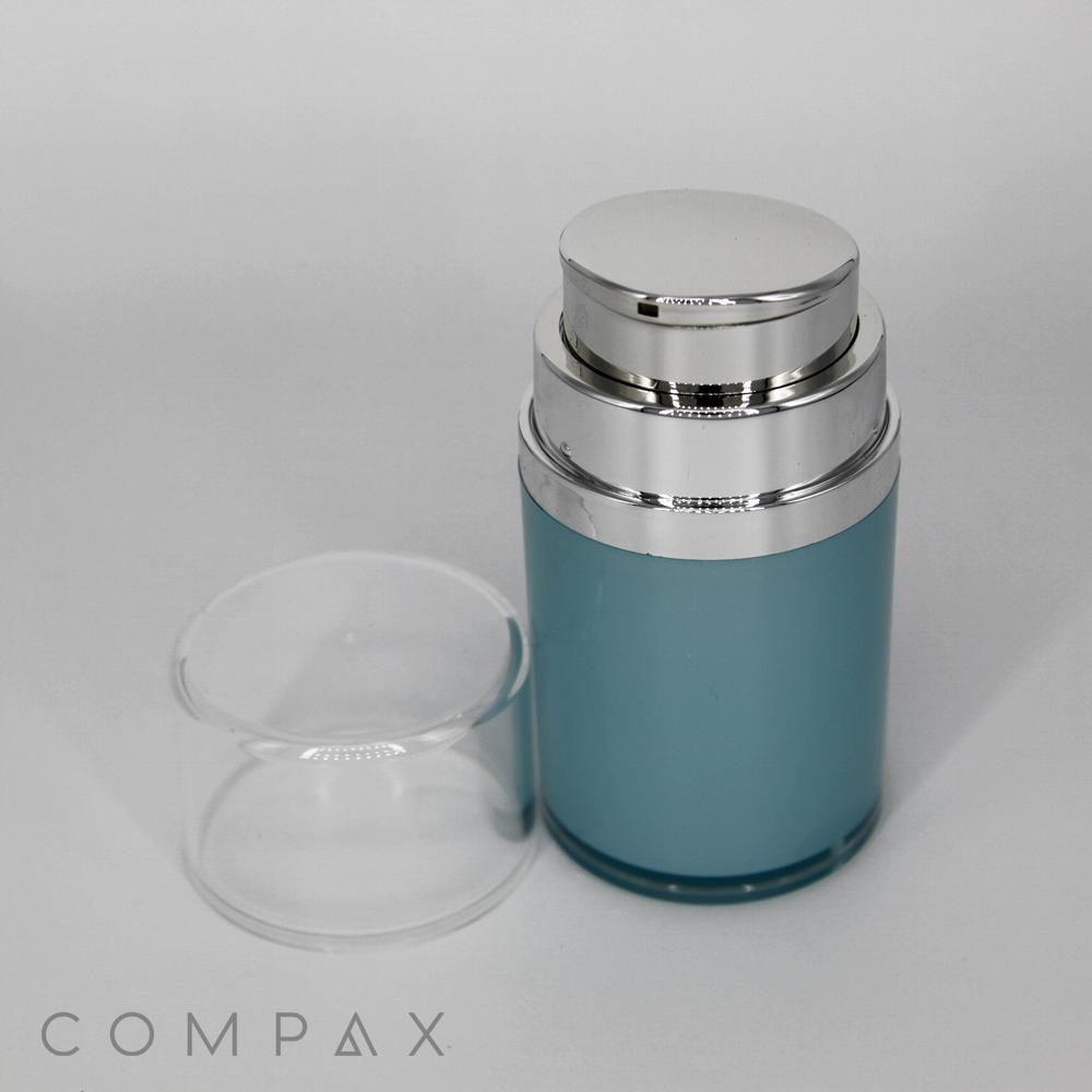 A Squatted Round Airless Bottle, blue in color with a silver pump dispenser on top and a clear plastic cap placed beside it. The container is labeled "COMPAX" in the bottom left corner, set against a plain white background.