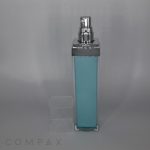A tall, rectangular Square Airless Bottle with a silver spray nozzle and a transparent cap, partially filled with a light blue liquid. The bottle is standing against a plain gray background, with the brand name "COMPAX" faintly visible at the bottom left corner.