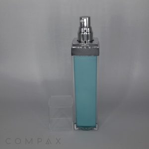 A tall, rectangular Square Airless Bottle with a silver spray nozzle and a transparent cap, partially filled with a light blue liquid. The bottle is standing against a plain gray background, with the brand name "COMPAX" faintly visible at the bottom left corner.