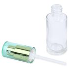 A small, clear 28mL Glass Cylinder Round Bottle lies on its side next to its detached spray cap with a metallic green and blue finish. The cap has a white plastic tube attached. The word "COMPAX" is visible at the bottom left corner of the image.