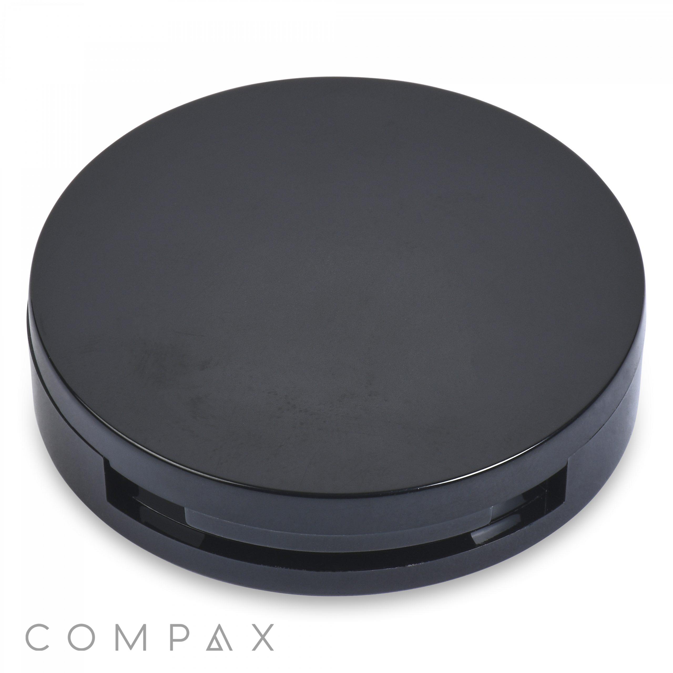 A sleek, black, circular compact case of the Round Platform Single Pan Eyeshadow Compact is shown against a white background. The item is closed, and the lid appears glossy with a subtle reflection. The brand name "COMPAX" is visible in light gray text at the bottom left corner of the image.