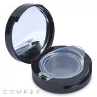 A round black compact case, the Airtight Eyeshadow Compact, is open, revealing an empty clear plastic compartment along with a built-in mirror on the inside of the lid. The word "COMPAX" is displayed in light gray at the bottom-left corner of the image.
