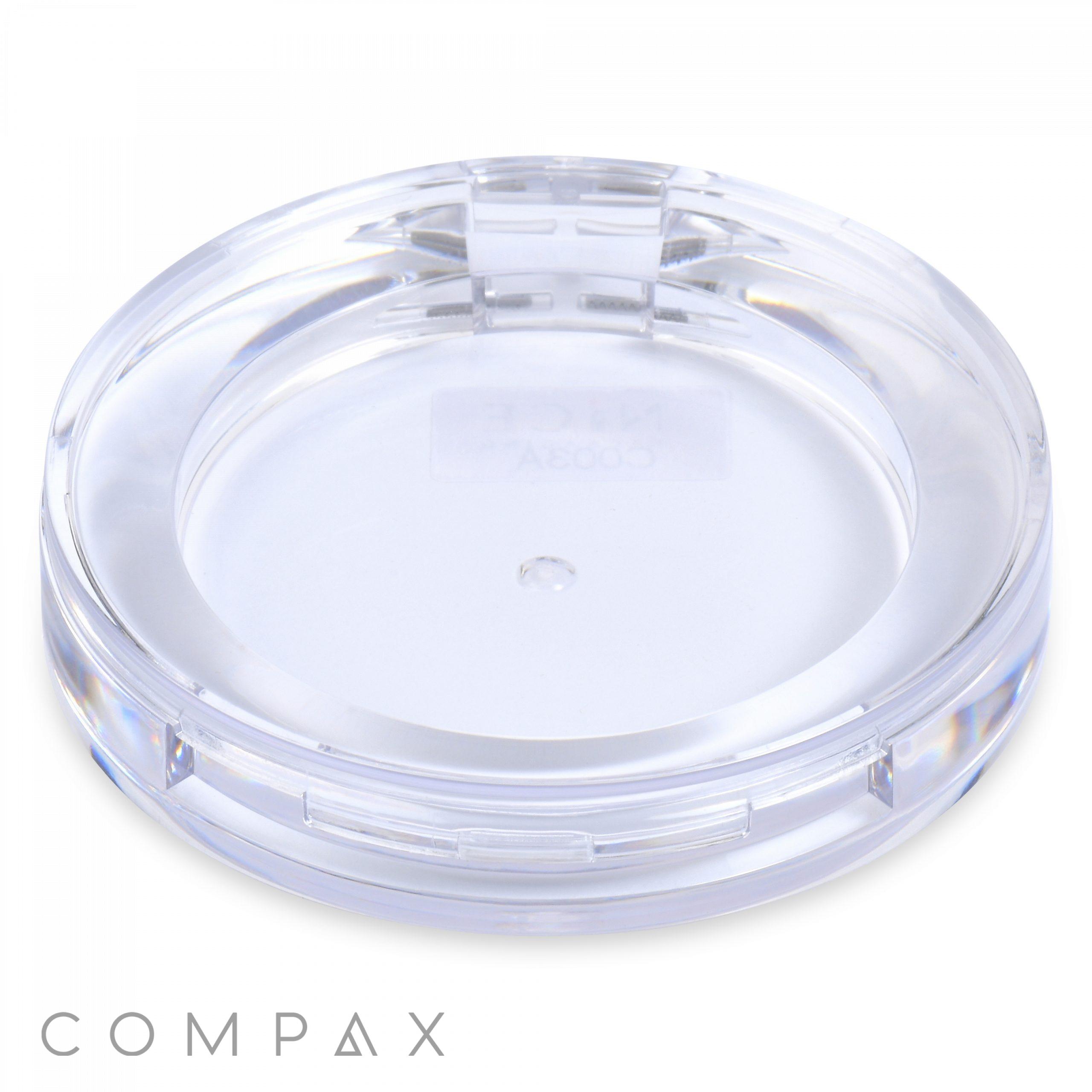 A clear, round, shallow plastic container with a smooth surface and a latch for sealing. The brand name "COMPAX" is visible at the bottom left corner. This Round Single Pan Eyeshadow Compact appears to be empty and is designed for holding small items or cosmetics.