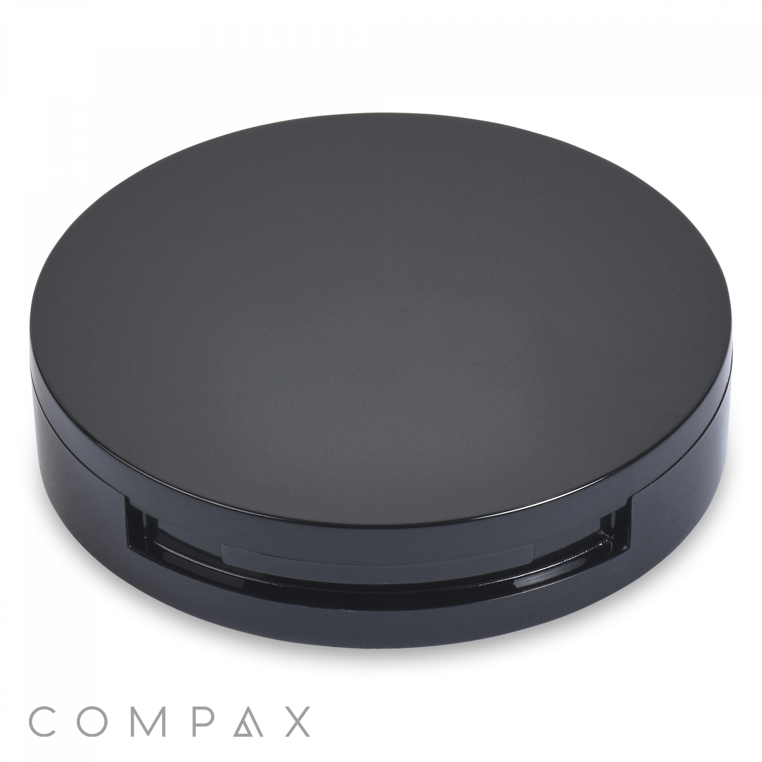 A sleek, black Round Single Pan Blush Compact with a glossy finish sits against a white background. The bottom edge has a slight opening, likely the hinge for opening the case. The brand name "COMPAX" is written in a minimalist font in the bottom left corner.