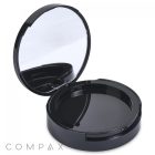 A sleek and modern, black circular Round Single Pan Compact with Brush Well is shown with its lid open to reveal an interior mirror at the top. The base of the compact is empty, containing no product. At the bottom left corner, "COMPAX" is displayed in light gray text.