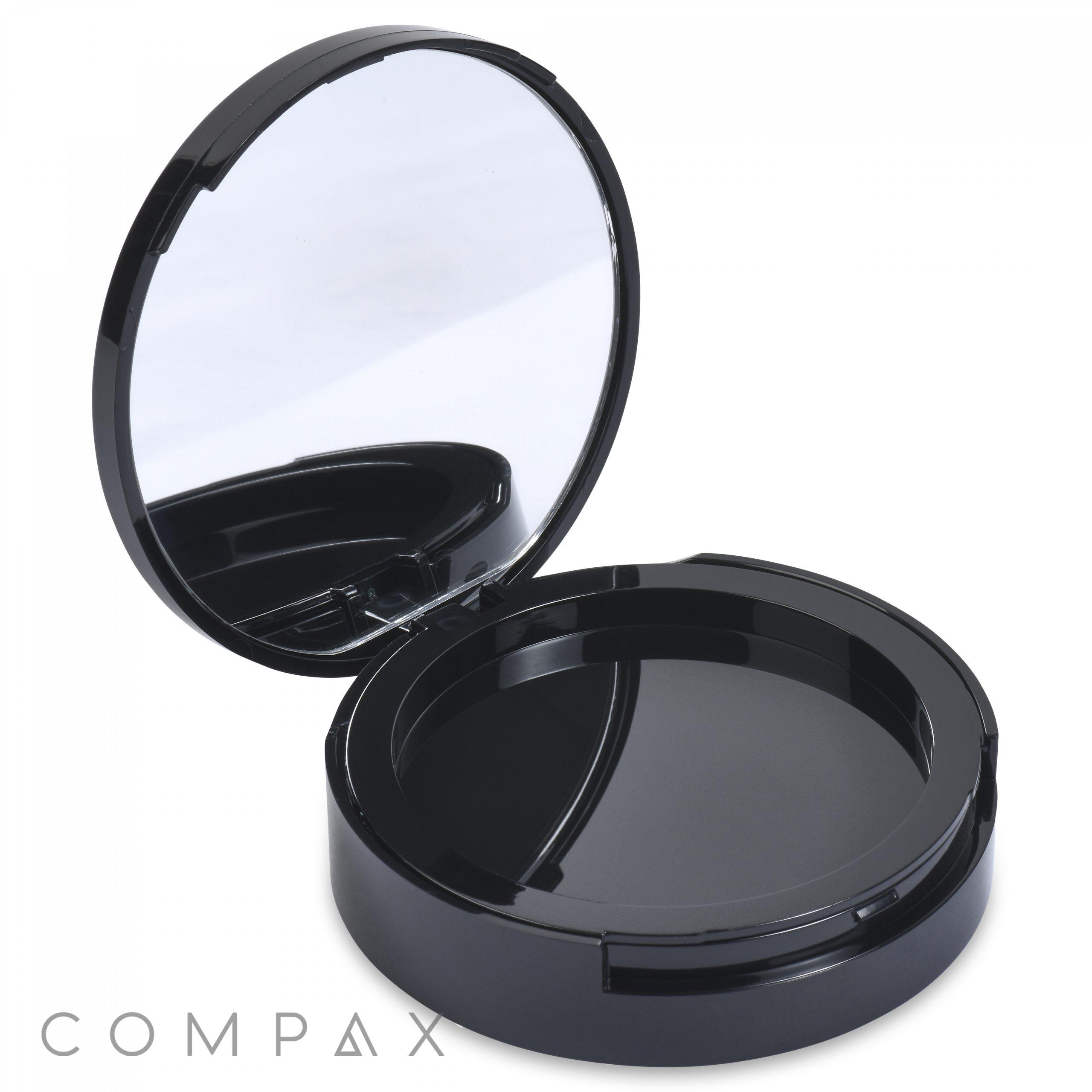 A sleek and modern, black circular Round Single Pan Compact with Brush Well is shown with its lid open to reveal an interior mirror at the top. The base of the compact is empty, containing no product. At the bottom left corner, "COMPAX" is displayed in light gray text.