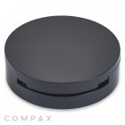 A sleek, round, black plastic container with a closed lid, likely for cosmetics or personal care products. The container has a subtle notch and the word "COMPAX" is visible in the bottom left corner. Named the "Round Single Pan Compact with Brush Well," it stands out against the white background, contrasting elegantly with its dark color.