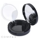 A black, round compact case known as the Round Airtight Compact is shown open, revealing an empty inner compartment and a built-in mirror on the inside of the lid. The hinged lid features a clear, protective cover and displays the brand name "COMPAX" in the lower left corner.