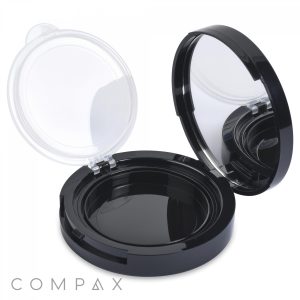 A black, round compact case known as the Round Airtight Compact is shown open, revealing an empty inner compartment and a built-in mirror on the inside of the lid. The hinged lid features a clear, protective cover and displays the brand name "COMPAX" in the lower left corner.
