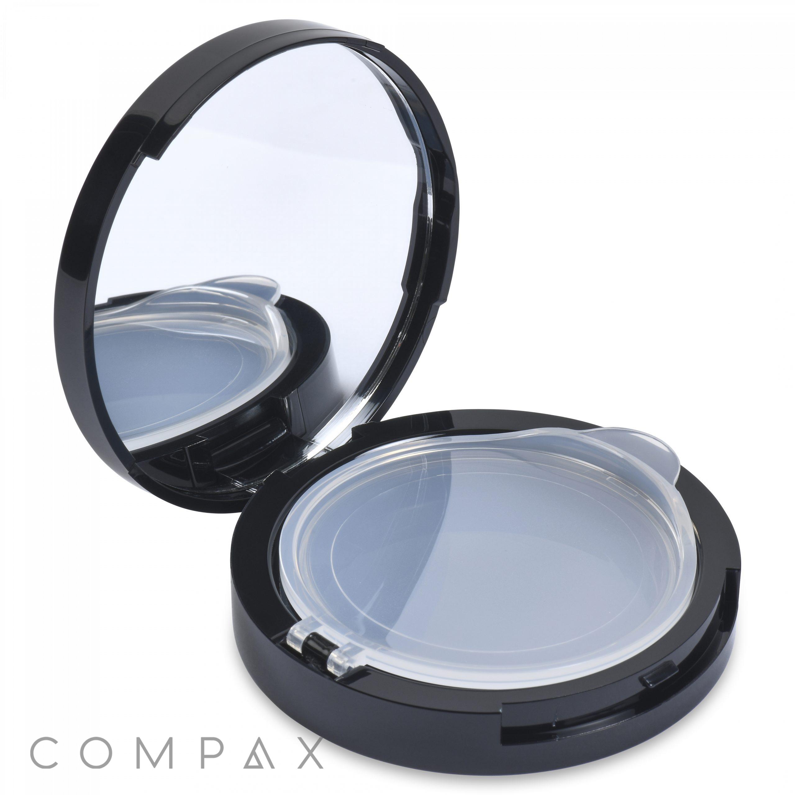 A black Round Airtight Compact case with an open lid revealing a clear plastic cover over an empty pan, designed to hold makeup. The underside of the lid features a mirror for convenient application. The word "COMPAX" is printed in gray at the bottom left corner.