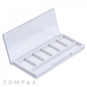 An open, square white plastic container labeled "Square Six Pan Eyeshadow Compact," featuring a transparent lid with six compartments arranged in two rows. The word "COMPAX" is visible in the bottom left corner.