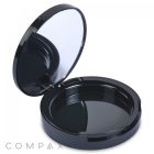 A sleek black, round Single Pan Compact case with an open design, featuring a mirror on the inside of the lid. The base of the case is empty and has a shiny finish. The brand name "COMPAX" is visible in the bottom left corner.