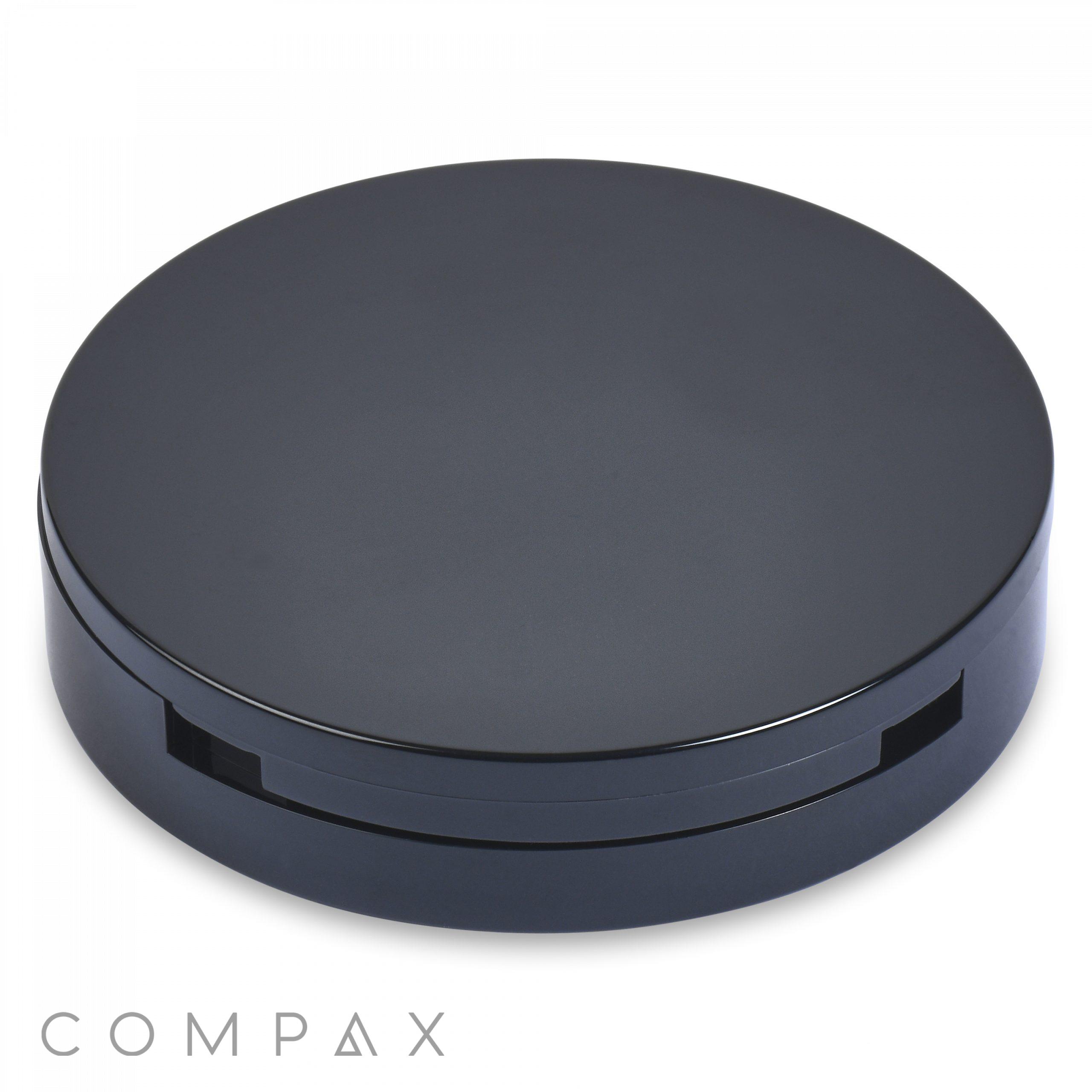 A sleek, round, black "Single Pan Compact" case with a minimalist design. The case is closed and boasts a smooth, glossy finish. "COMPAX" is inscribed in light gray text at the bottom left corner of the image.