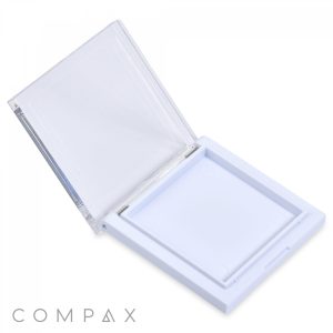 A Square Single Pan Compact, featuring a white square plastic design and a hinged transparent lid, is open to display its empty shallow compartment. The brand name "COMPAX" is printed in gray near the bottom left corner of the image.