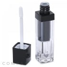 A square clear lip gloss tube with a black cap. When the cap is removed, it reveals a white applicator wand attached. The tube contains clear gloss and the brand name "COMPAX" is subtly printed at the bottom of the image.
