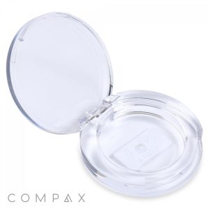 A clear, open Round Single Pan Eyeshadow Compact features a simple, circular design. The lid is hinged at the back, and the transparent base reveals the word "COMPAX" in white inside the case. The background is plain white, with the brand name "COMPAX" displayed in the bottom left corner of the image.
