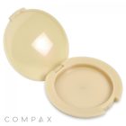 A beige Round Single Pan Compact is open, displaying a matching interior where the powder can be stored. The case features a hinge at the back and a latch at the front. The word "COMPAX" is printed on the bottom left corner of the exterior.
