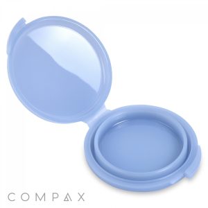 A blue, round, empty "Round Single Pan Compact" with a hinged cover is shown open. The compact has a mirrored lid, and the brand name "COMPAX" is visible in the lower left corner.