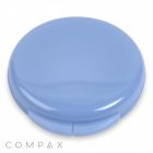 A round Single Pan Compact case in light blue with a glossy finish, closed and resting on a white surface. The word "COMPAX" is written in gray capital letters at the bottom left corner of the image.