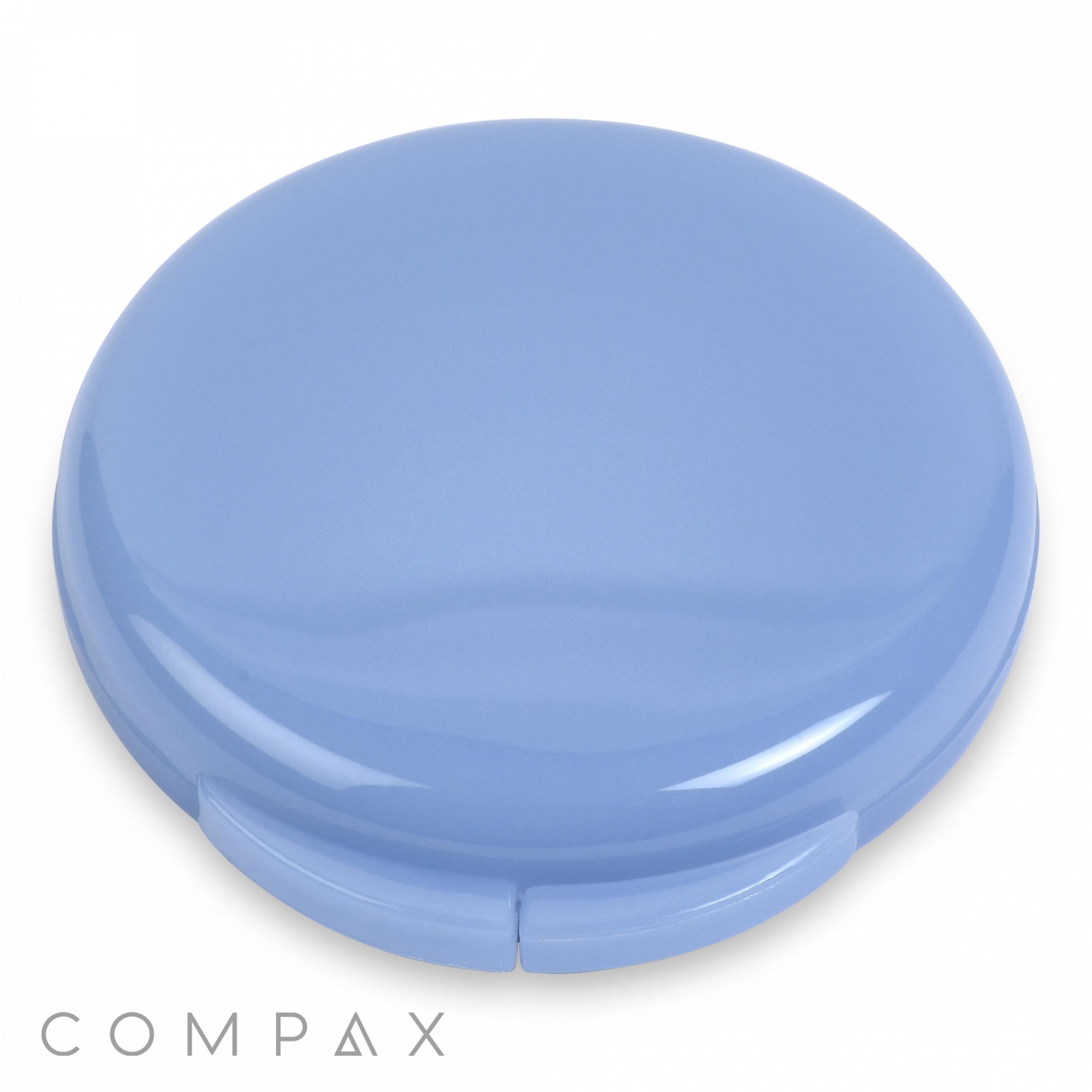 A round Single Pan Compact case in light blue with a glossy finish, closed and resting on a white surface. The word "COMPAX" is written in gray capital letters at the bottom left corner of the image.