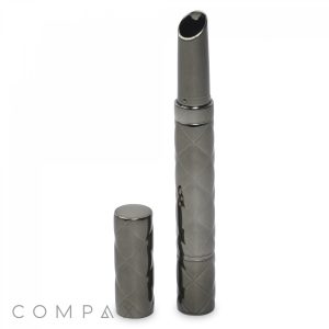 A sleek, metallic, cylindrical Round Lipstick stands upright on a white background. The device has a quilted pattern and is shown with its cap placed next to it. The brand name "COMPAX" appears in small letters in the bottom left corner.