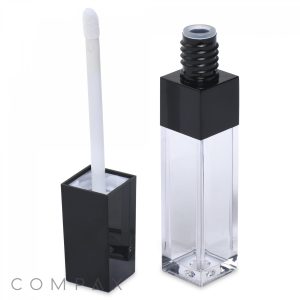 A clear square lip gloss tube with black accents is shown. The tube has a black cap and is open to reveal a white applicator wand. The word "COMPAX" is written at the bottom left corner of the image.