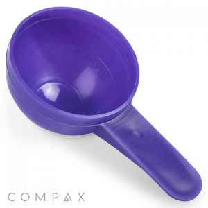 A 20cc purple plastic scoop with a rounded bowl and a flat handle on a white background. The word "COMPAX" is printed in the bottom left corner.