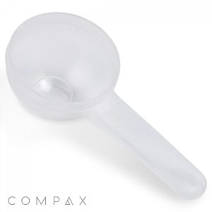 A translucent plastic 20cc Scoop with a long handle and a round bowl is depicted on a white background. The scoop features measurement markings on the side, and the word "COMPAX" appears in the bottom left corner of the image.