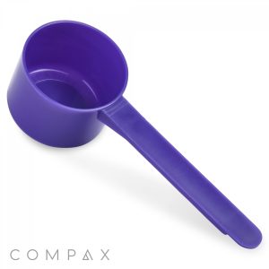 A purple plastic 48cc measuring scoop with a long handle is positioned against a white background. The word "COMPAX" is printed in light gray at the bottom left corner.