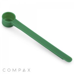 A 5cc Scoop made of green plastic with a long handle. The cylindrical scoop is attached to the handle and used for measuring powdered or granulated substances. The word "COMPAX" is visible in grey text at the bottom left corner.